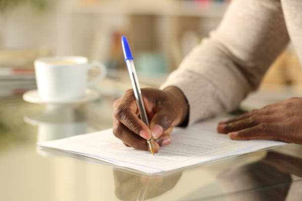 Close up of a black man hands filling out form on a desk at home